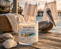 Harbor Morning Co. Dockside Linen 8oz hand-poured coastal soy candle lit on the docks with a pelican, linen hanging on an outdoor line, and ocean in the background