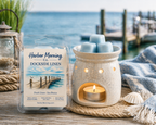 Harbor Morning Co. Dockside Linen coastal wax melts on a dock with nautical lantern, wax warmer, sea grass, seashells, towel, and ocean in the background