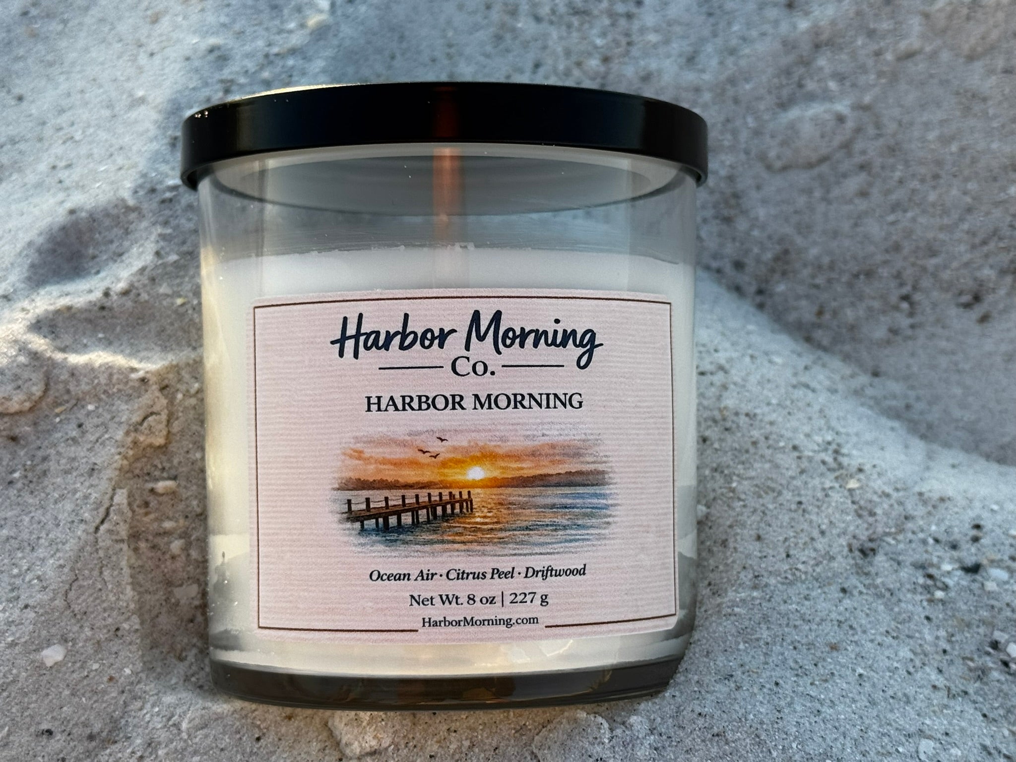 Harbor Morning Co. candle label sitting in the beach sand on Madeira Beach Florida