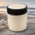 Harbor Morning Co. signature 4oz hand-poured coastal soy candle on driftwood with sea grass, morning sunshine, and a pier in the background