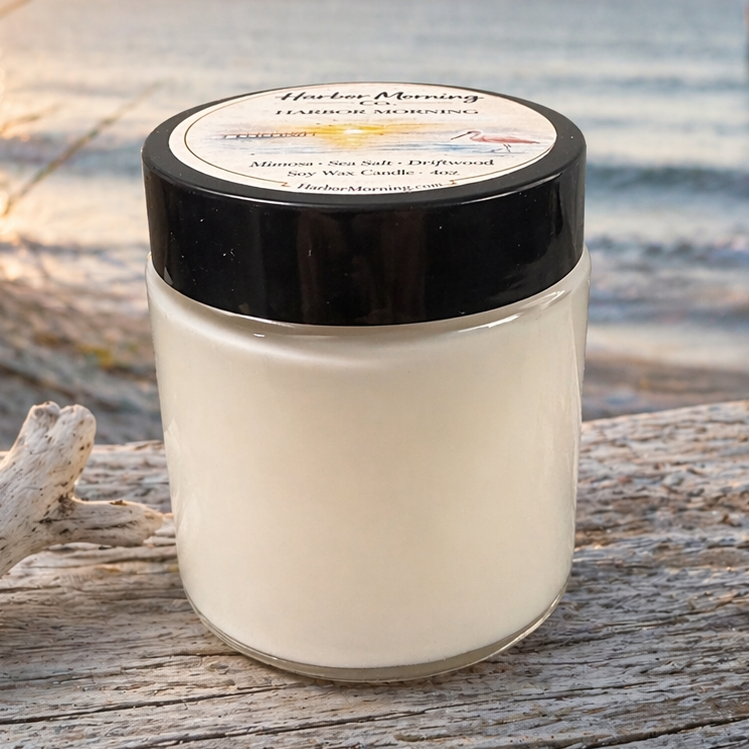 Harbor Morning Co. signature 4oz hand-poured coastal soy candle on driftwood with sea grass, morning sunshine, and a pier in the background