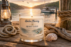 Harbor Morning Co. Quiet Cove 8oz hand-poured coastal soy candle lit on a pier alongside a nautical lantern with fishing boat and coastal sunrise in the background