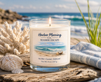 Harbor Morning Co. Seaside Escape 4oz hand-poured coastal soy candle lit and seated on driftwood with a towel, seashells, and seagrass in the background